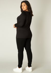 Zwarte top met lange mouwen en zwarte leggings, beide in een aansluitend ontwerp. De top heeft een ronde halslijn en is gecombineerd met witte sneakers.