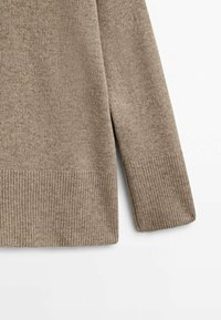 Beżowy sweter dzianinowy z akcentem na rękawie i dolnej krawędzi, ukazujący teksturalne detale ściągacza przy mankiecie i dolnej krawędzi na białym tle.