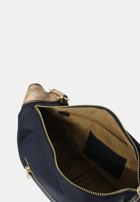 Borsa in tessuto blu navy con tracolla in pelle beige. La chiusura con cerniera dorata rivela un interno beige con una tasca piccola e un'etichetta del marchio.