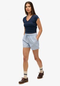Navy bomulds T-shirt med korte ærmer og V-udskæring; lyseblå stribede shorts med elastisk talje og lommer; brune sko med snørebånd.