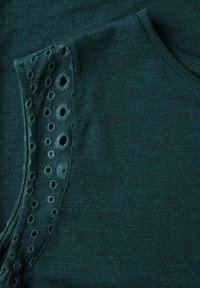 Donker teal gebreide top met geborduurde oogletdetails op de schouder, een gladde textuur en een klassieke ronde halslijn.