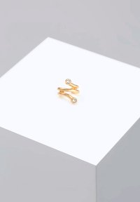 Goldfarbener, gedrehter Ring mit zwei kleinen, klaren Steinen. Glatte Textur mit einem minimalistischen Design, vor einem hellen Hintergrund.