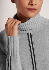 Grauer Rollkragenpullover mit geripptem Kragen und Bündchen, ausgestattet mit zwei senkrechten schwarzen Streifen an den Seiten für zusätzlichen Detail.