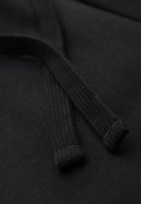 Gros plan d'un tissu noir tissé avec deux extrémités de cordon texturées reposant sur la surface.