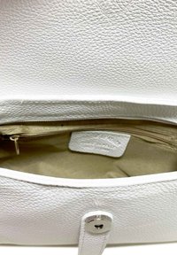 L'interno della borsa in pelle bianca presenta una tasca con zip, foderato in beige e un'etichetta identificativa. L'esterno ha una superficie texture e ferramenta in argento.