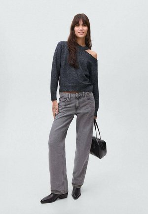 Maglione off-shoulder metallico nero, jeans grigi a vita alta con dettagli perforati e stivaletti neri. Tieni una piccola borsa nera.