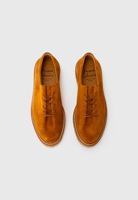 Une paire de chaussures en suede marron à lacets avec des semelles cousues, disposées côte à côte sur un fond blanc.