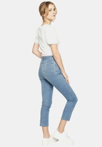 Jasnoniebieskie dżinsy o slim fit, skróconej długości i postrzępionym wykończeniu. Noszone z białym topem z krótkim rękawem i białymi tenisówkami.