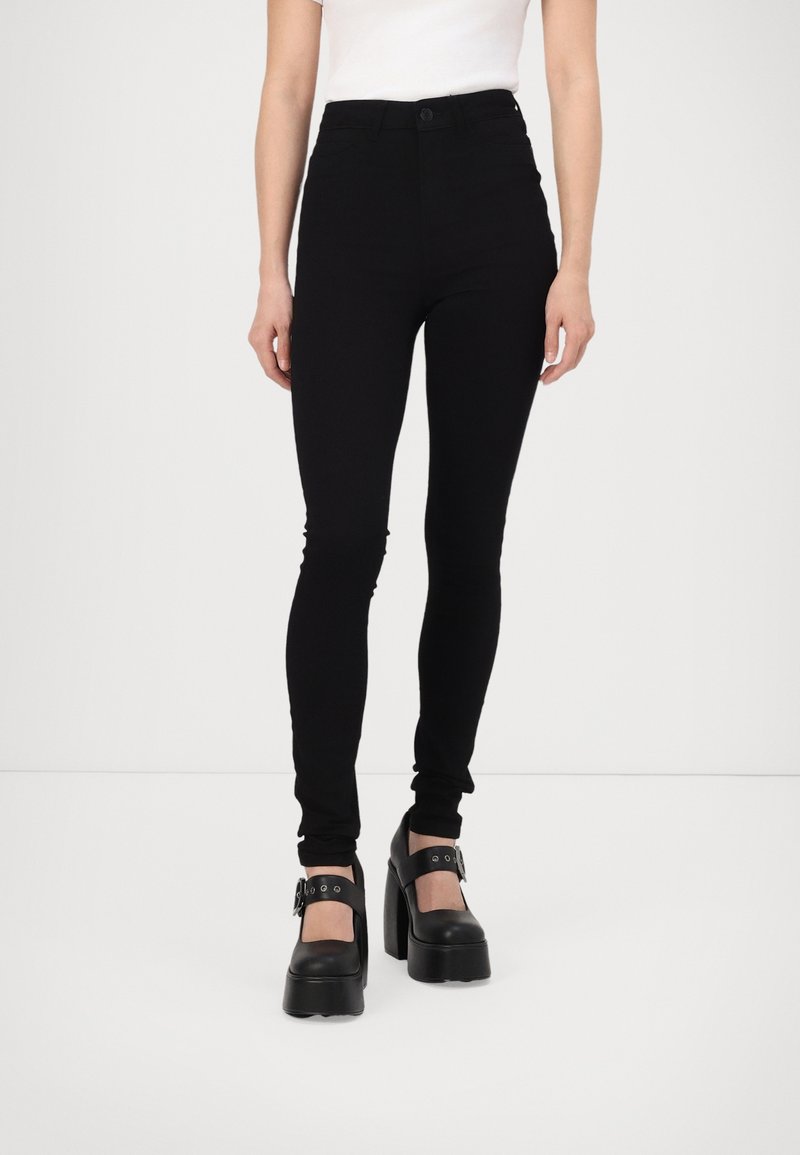 Black high-waisted leggings in a stretchy fabric. Features a button closure and a slim fit, paired with chunky black platform shoes.