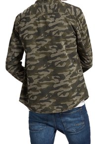 Camicia con motivo camouflage nei toni del verde e marrone, realizzata in tessuto con una vestibilità comoda, caratterizzata da un orlo curvo e un design casual, abbinata a jeans blu.