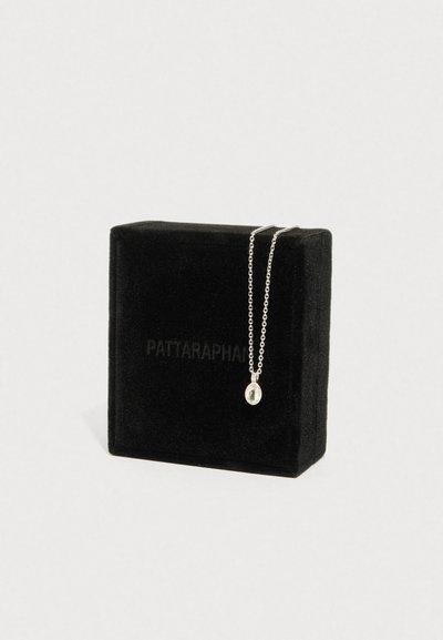 Stříbrný náhrdelník s oválným přívěskem z průhledného kamene položený přes černou sametovou čtvercovou šperkovnici na bílém pozadí.