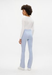 Leggings fitted di un azzurro chiaro con fondo svasato, realizzati in tessuto elasticizzato, abbinati a una maglietta bianca a maniche lunghe. Design semplice con una texture liscia.
