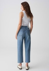 Jeans azzurri a vita alta con gamba dritta, dotati di tasche posteriori e una finitura testurizzata, abbinati a un top bianco senza maniche.