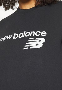 Svart bomulls-t-shirt med vit "new balance" text och logotyp. Rund halsringning och korta ärmar. Slät textur, avslappnad design.