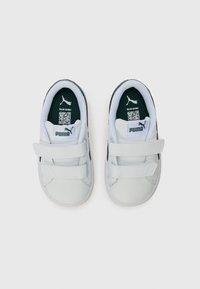 White sneakers with black accents, featuring a smooth synthetic upper, two Velcro straps, and a green inner lining with a logo.