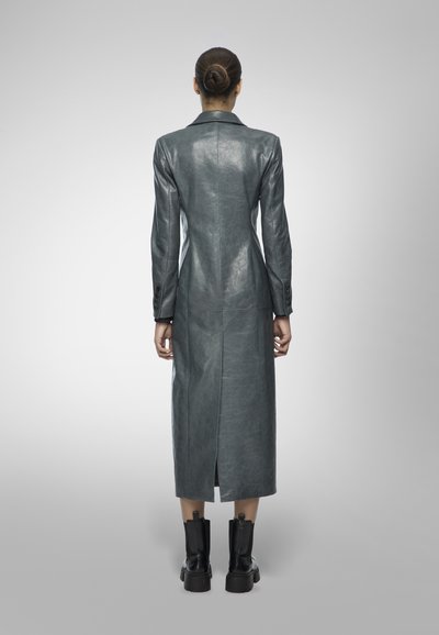 Long gray leather coat with a back vent, structured shoulders, and buttoned cuffs, paired with black chunky-heeled ankle boots.