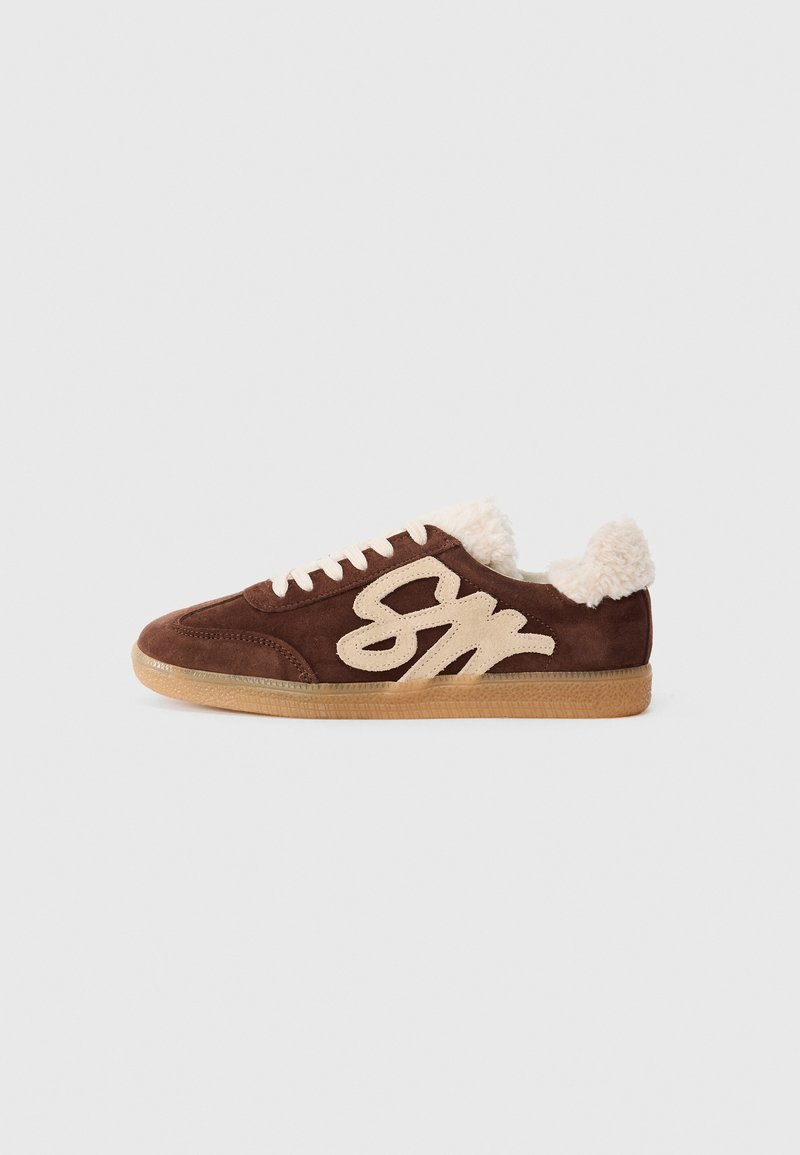 Brown suede sneaker with cream-colored faux fur lining and a prominent beige logo. Features white laces and a textured gum sole.