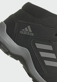 Chaussure de sport noire avec une tige synthétique texturée, des accents gris, le logo à trois bandes et une semelle extérieure en caoutchouc durable.