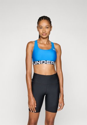 Blauwe sportbeha met een zwarte elastische band met de tekst "UNDER", gecombineerd met hoge zwarte shorts. Soepele, aansluitende pasvorm.