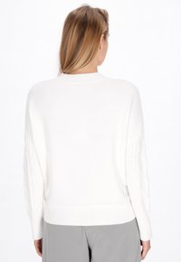 Pulover alb din tricot cu tiv ondulat și modele de diamante 3D pe mâneci. Croi lejer și textură moale, având un decolteu rotund.