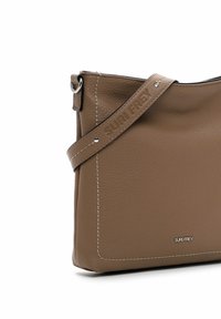 Brown leather crossbody bag with a textured surface, white stitching, and a branded strap. Features a sleek, modern design.