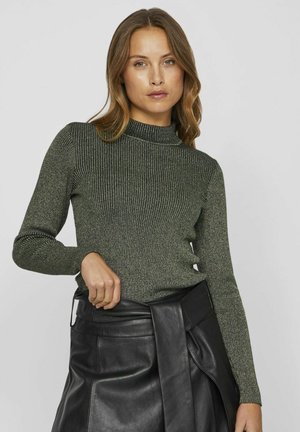 Suéter de cuello alto acanalado verde con mangas largas, tejido texturizado y diseño ajustado, combinado con una falda corta de cuero negro con un detalle de lazo.