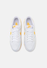 Weiße Sneaker mit perforierter Zehenbox, gelben Akzenten und einer strukturierten Gummisohle. Schnürsenkel und gepolsterter Kragen für einen sicheren Sitz.