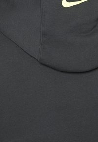 Sudadera gris oscuro hecha de un tejido suave, con una textura acanalada. El logo de Nike está destacado en un brillante color amarillo.