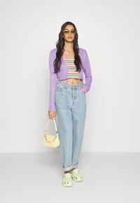 Cardigan cropped em malha roxa, top cropped às riscas multicolorido, jeans baggy azul claro, mala amarela e tamancos verdes.