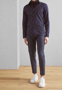 Marinblus med vitt geometriskt mönster, lång ärm; kombinerad med skräddarsydda mörka byxor och vita sneakers. Enkel design, texturerad tyg.