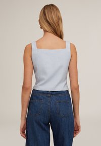 Ljusblå, strukturerad ärmlös topp med fyrkantig halsringning. Matchad med högmidjade mörka denimjeans med bakfickor.
