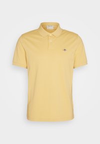 Gul bomullspiké med klassisk krage, korta ärmar, framsidan med knappslå och en liten broderad logotyp på bröstet.