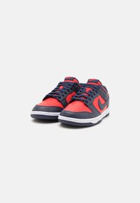 Sneakers Nike con tomaia blu navy, dettagli rossi, punta perforata e suola bianca. Presentano lacci tondi e logo distintivo sui lati.