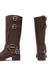 Cizme maro până la genunchi, cu un finisaj neted, având trei accente cu catarame pe tijă, o curea solidă și un toc pătrat.