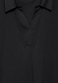 Schwarzes Polohemd aus glattem Stoff, mit einem Zwei-Knopf-Bund, umgeschlagenem Kragen und genähten Details am Halsauschnitt.