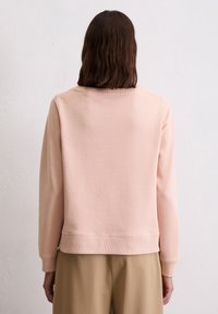Lichtroze sweatshirt met ribbels aan de manchetten en onderrand. Zachte stof, relaxte pasvorm en ronde halslijn zichtbaar vanaf de achterkant. Gecombineerd met beige broek.