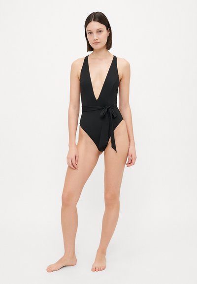 Black one-piece swimsuit with a deep V-neck and tie detail at the waist. Smooth fabric with high-cut legs and a minimalist design.