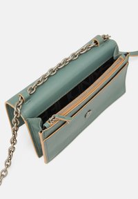 Borsa a tracolla in pelle verde con catena, dotata di uno scomparto con zip e accenti beige lungo i bordi. Superficie texturizzata, interno con motivo.