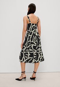 Robe sans manches noire et crème avec un corsage ajusté, une jupe évasée, un motif abstrait et un détail de nœud papillon dans le dos.