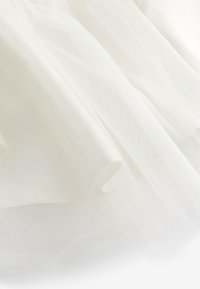 Tissu blanc doux et transparent avec une texture délicate en maille fine, drapé doucement pour créer des plis fluides et des ombres légères.