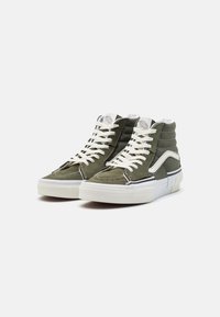 Høye sneakers i olivengrønn semsket skinn med hvite snøringer og gummisåler, med brodert logo og kontrastdetalj i svart stripe.