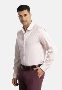 Camisa de botones rosa claro con un patrón sutil, de mangas largas y un cuello clásico; combinada con pantalones burdeos oscuros y un cinturón negro.