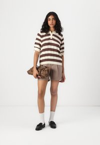 Stripet strikket polo skjorte i krem og brunt, sammen med beige shorts; holder en brun, samlet håndveske; svarte sko og hvite sokker.