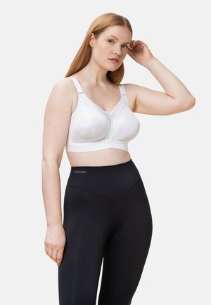 Reggiseno wireless bianco con scollatura a V, decorazioni in pizzo e spalline larghe, abbinato a leggings neri a vita alta con logo laterale.