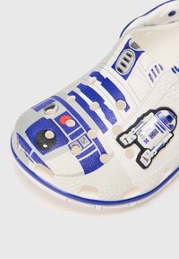 Vaikų balti šlepečiai su mėlynu ir pilku R2-D2 roboto dizainu ir ventiliacijos angomis viršutinėje dalyje.