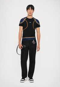 Camiseta negra ajustada con costuras azules y naranjas, combinada con pantalones negros texturizados. Los accesorios incluyen un bolso pequeño con una correa.