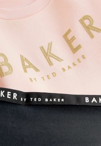 Sweatshirt rose avec le texte doré "BAKER", un bas noir et un accent en ruban de marque. Tissu doux, col rond et couleurs contrastées.