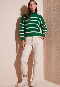 Maglione a righe verdi e bianche lavorato a maglia con colletto alto, abbinato a pantaloni crema e stivali alla caviglia bianchi. Tessuto testurizzato, vestibilità rilassata.