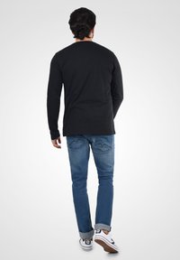 Sort langærmet skjorte kombineret med lyseblå jeans og hvide sneakers. Jeansene har en subtil zigzag syning detalje på lommerne.