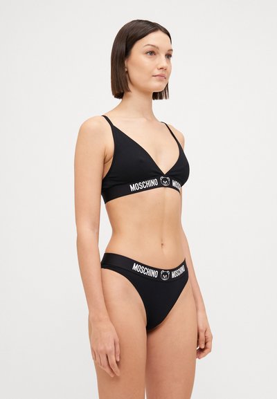 Crni bikini set koji se sastoji od trokuta brusa s tankim trakama i hlačica viskog struka. Obje komponente imaju bijelu elastičnu traku s brandom.